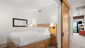 Una habitación de hotel con una cama de madera, una mesita de noche con lámpara, un espejo y un armario de madera.