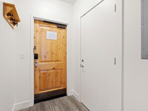 A wooden door with a small sign, a white wall, and a metal fixture above it.