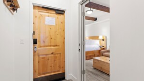 Hotellihuone, jossa on puinen ovi, sängyssä on pääty ja huoneessa on yöpöytä sekä lamppu.