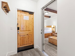 Ein Hotelzimmer mit Holztür, einem Bett mit Kopfteil, einem Nachttisch und einer Lampe.