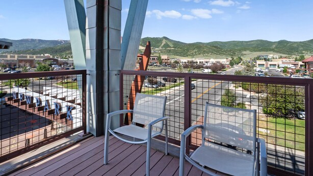 Ein Balkon mit zwei Metallstühlen, Blick auf einen Parkplatz, Gebäude und Berge im Hintergrund.