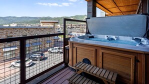 Un balcon avec un jacuzzi, une terrasse en bois et une vue sur un parking et des immeubles.