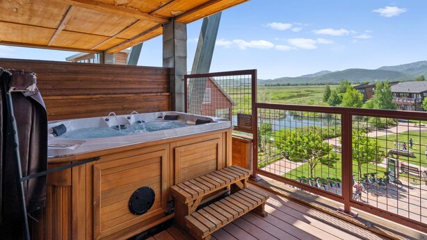 Tinaja de madera con escalones, una terraza de madera y vistas a un río y montañas.