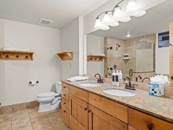 Un baño moderno con dos lavamanos, armarios de madera, un espejo grande y toalleros.