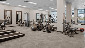 A gym with various exercise equipment, large windows, and a carpeted floor.