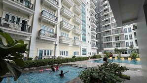 A multi-story residential building with balconies, a swimming pool area with people, and greenery. - Room-cozy Iloilo City Condo Room With Sh (Iloilo)