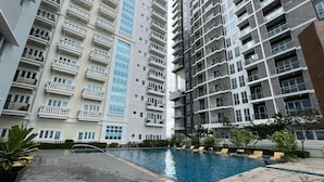 A high-rise residential building with multiple balconies, a swimming pool, and surrounding greenery. - Room-cozy Iloilo City Condo Room With Sh (Iloilo)