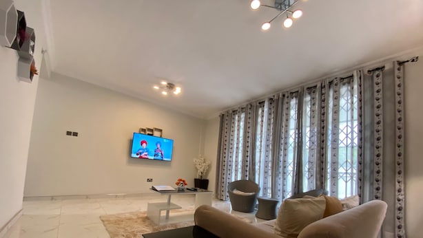 Ein modernes Wohnzimmer mit Flachbildfernseher, einer Couch, einem Couchtisch und einem dekorativen Sessel.