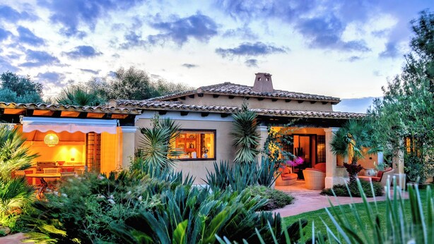 Una casa in stile mediterraneo con patio, arredi da esterno e un rigoglioso giardino.