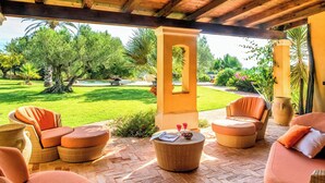 Patio esterno con mobili in vimini, pavimento in mattoni e vista su un giardino curato.
