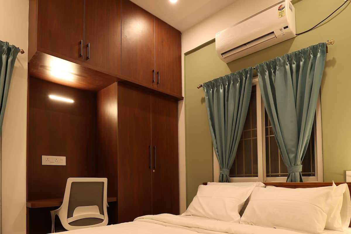 A bedroom with a bed, a chair, a wardrobe, and an air conditioning unit.