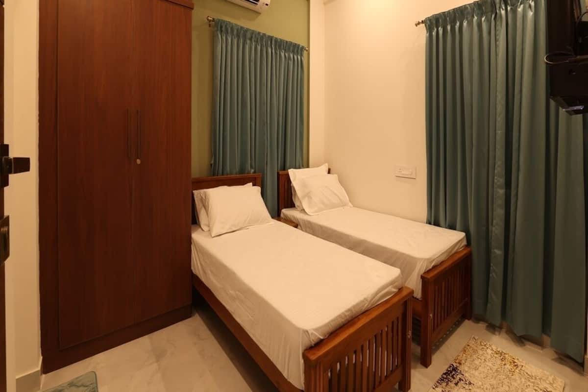 A bedroom with two single beds, a wardrobe, an air conditioning unit, and a television.