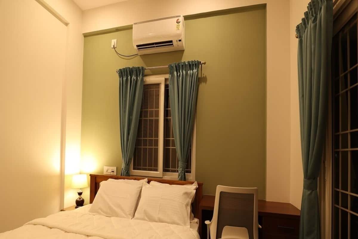 A hotel room with a bed, a chair, an air conditioning unit, and curtains.