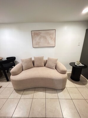 A living room with a beige sofa, a coffee table, and a painting on the wall. - AUREA Stays /Private 2BR Suite / Free Parking /Near EWR (Newark)