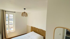 Un dormitorio con cama, ventana con cortinas, lámpara colgante y espejo en la pared.