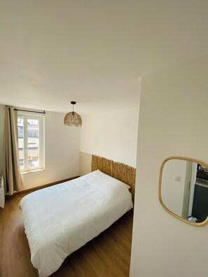 A bedroom with a bed, a window with curtains, a hanging light fixture, and a mirror on the wall.