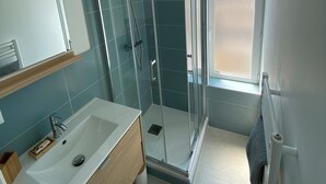 Un baño moderno con ducha de vidrio, lavamanos blanco y un espejo grande.
