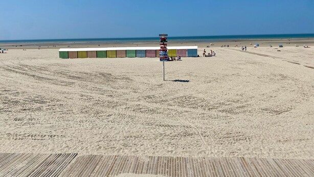 Una playa con una fila de coloridas cabañas playeras y un paseo marítimo de madera.