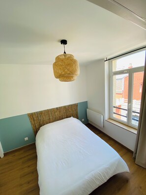A bedroom with a large bed, a window with a view, and a hanging light fixture.