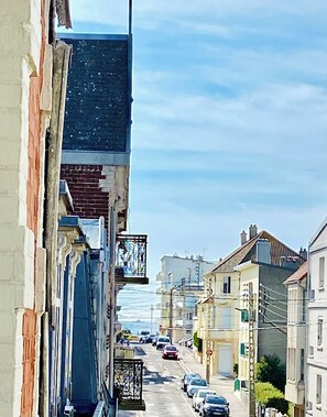 A narrow street with buildings on either side, a clear sky, and parked cars.