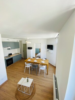 A modern kitchen with a dining area, a TV mounted on the wall, and a small table with a vase.