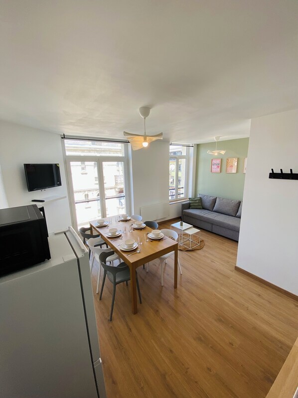 A modern living space with a dining area, a grey sofa, a flat-screen TV, and a wooden dining table set for four.