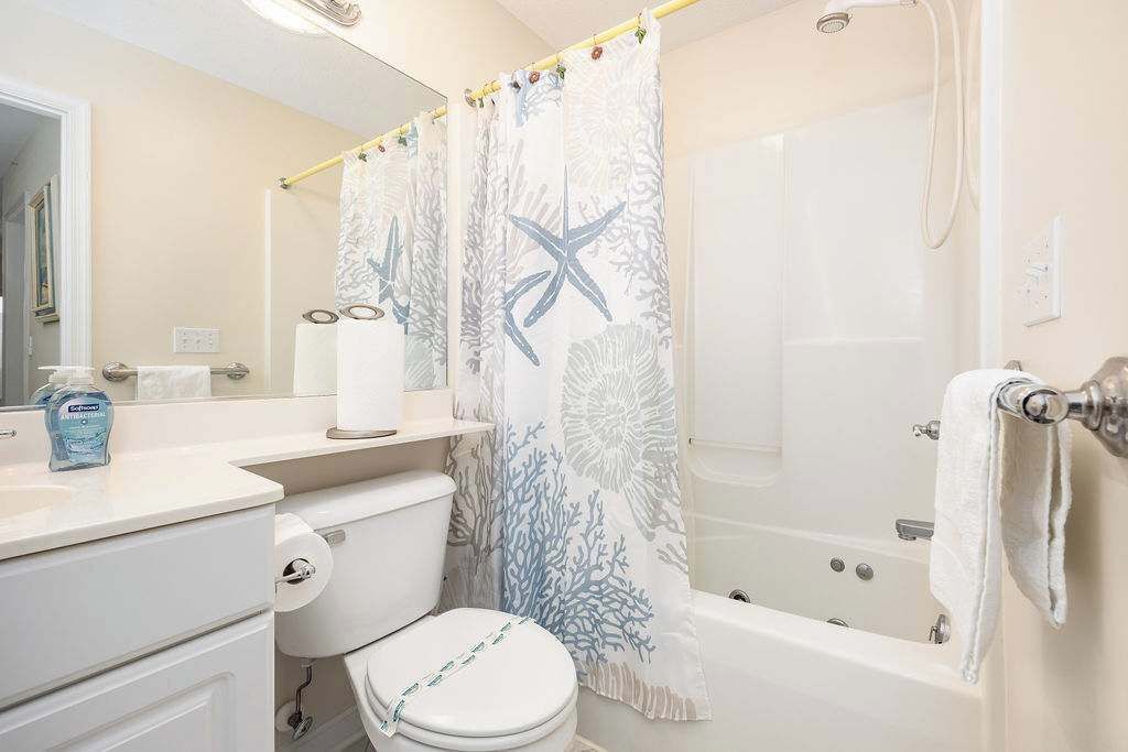 A bathroom with a toilet, a bathtub, and a shower curtain with a marine theme.