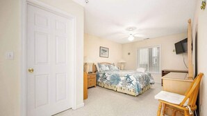 A bedroom with a bed, a chair, a desk, a television, and a ceiling fan.