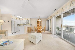 A spacious living area with a dining table and chairs, a kitchen with white cabinets, and a large sliding glass door to the outside.