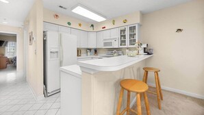 A kitchen with white cabinets, a white countertop, and two wooden stools.