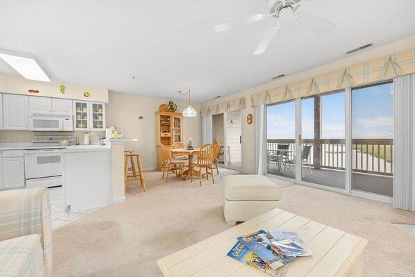 A spacious living area with a dining table, a sofa, and a balcony with large windows.