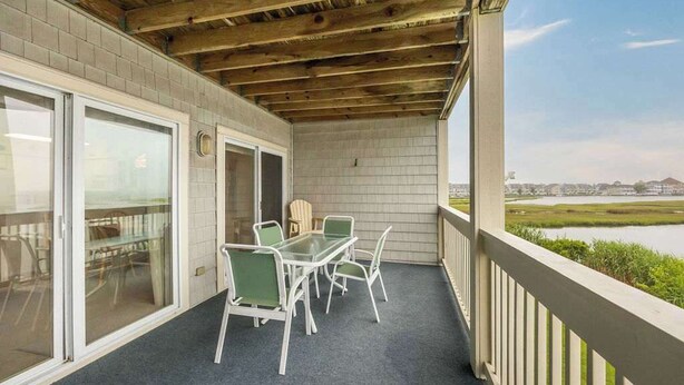A covered balcony with a table and chairs, a view of a body of water, and a brick wall.