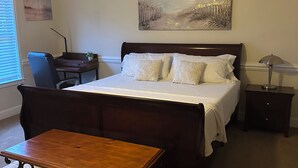 Un dormitorio con cama, mesitas de noche, escritorio, silla y una pequeña mesa.