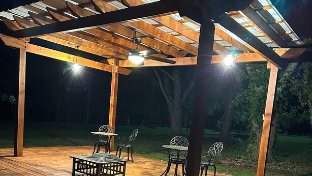 Una terraza de madera al aire libre con una pérgola, zona de estar y un ventilador de techo.