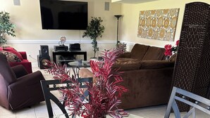 Una sala de estar con una mesa de centro de vidrio, dos sillones, un sofá, un televisor y un ventilador de techo.