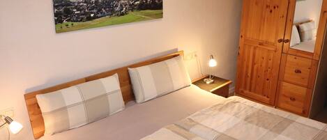 Een slaapkamer met een bed, nachtlampjes, een houten garderobe en een landschap op de muur.
