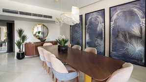 A modern dining area with a long wooden table, cushioned chairs, and large abstract wall art. - Easy Rental/ Serviced Apartment In Corniche El Maadi (Corniche El Maadi Cairo Governorate)