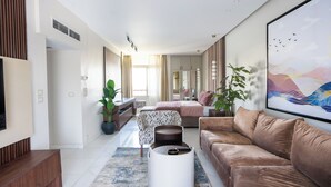 A modern living room with a brown leather sofa, a white coffee table, and a patterned armchair. There is a large window with curtains, a flat-screen TV mounted on the wall, and a framed artwork above the sofa. - Easy Rental/ Serviced Apartment In Corniche El Maadi (Corniche El Maadi Cairo Governorate)