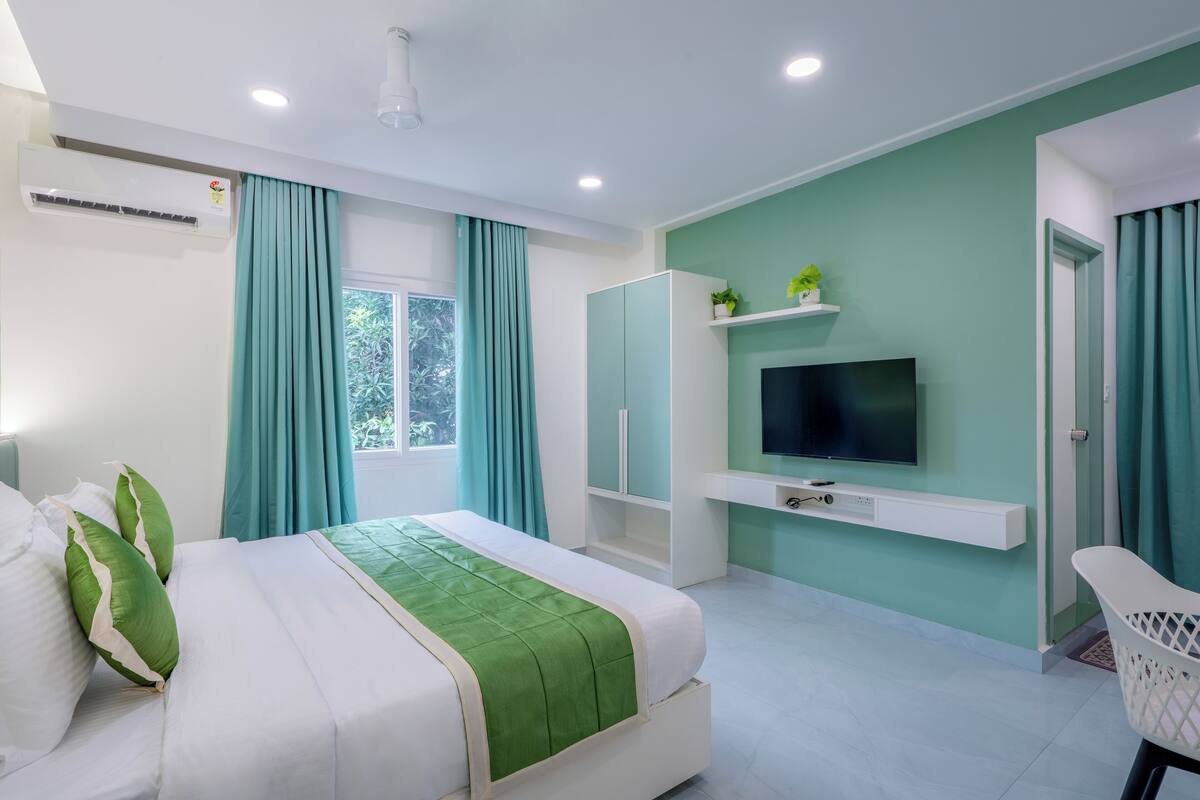 Ein modernes Hotelzimmer mit Bett, Wandfernseher, Kleiderschrank und einem Fenster mit Vorhängen.