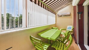 A small patio with a green table and chairs, a window with white blinds, and a view of trees. - 300m from beach, Andernos centre – sleeps 4 (Andernos-les-Bains)
