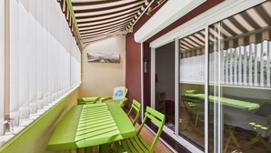 A patio with a green table and chairs, a striped awning, and a sliding glass door leading to a deck. - 300m from beach, Andernos centre – sleeps 4 (Andernos-les-Bains)