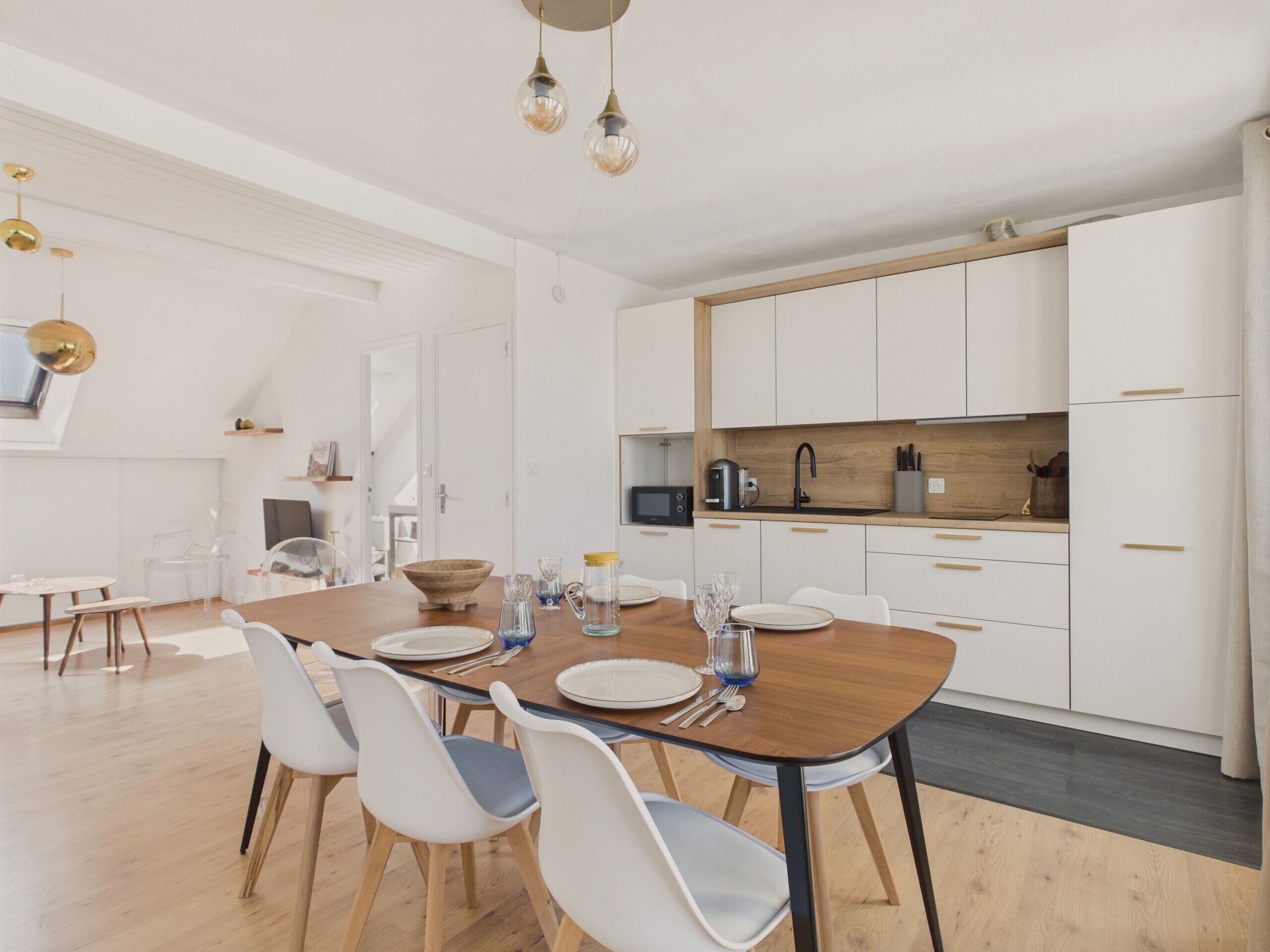 A modern kitchen with white cabinets, a wooden countertop, and a dining area with a wooden table and white chairs.