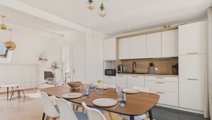 A modern kitchen with white cabinets, a wooden countertop, and a dining area with a wooden table and white chairs.