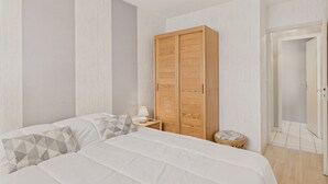 Ein Schlafzimmer mit einem großen Bett, einem Holzschrank, einem Nachttisch mit Lampe und einem kleinen Hocker.