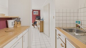 Eine schmale Küche mit weißen Schränken, einer Holz Arbeitsplatte, einem Wasserkocher und einem Spülbecken.