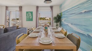 Un comedor con una mesa de madera preparada para seis personas, rodeado de sillas, con vistas al mar a través de grandes ventanales.