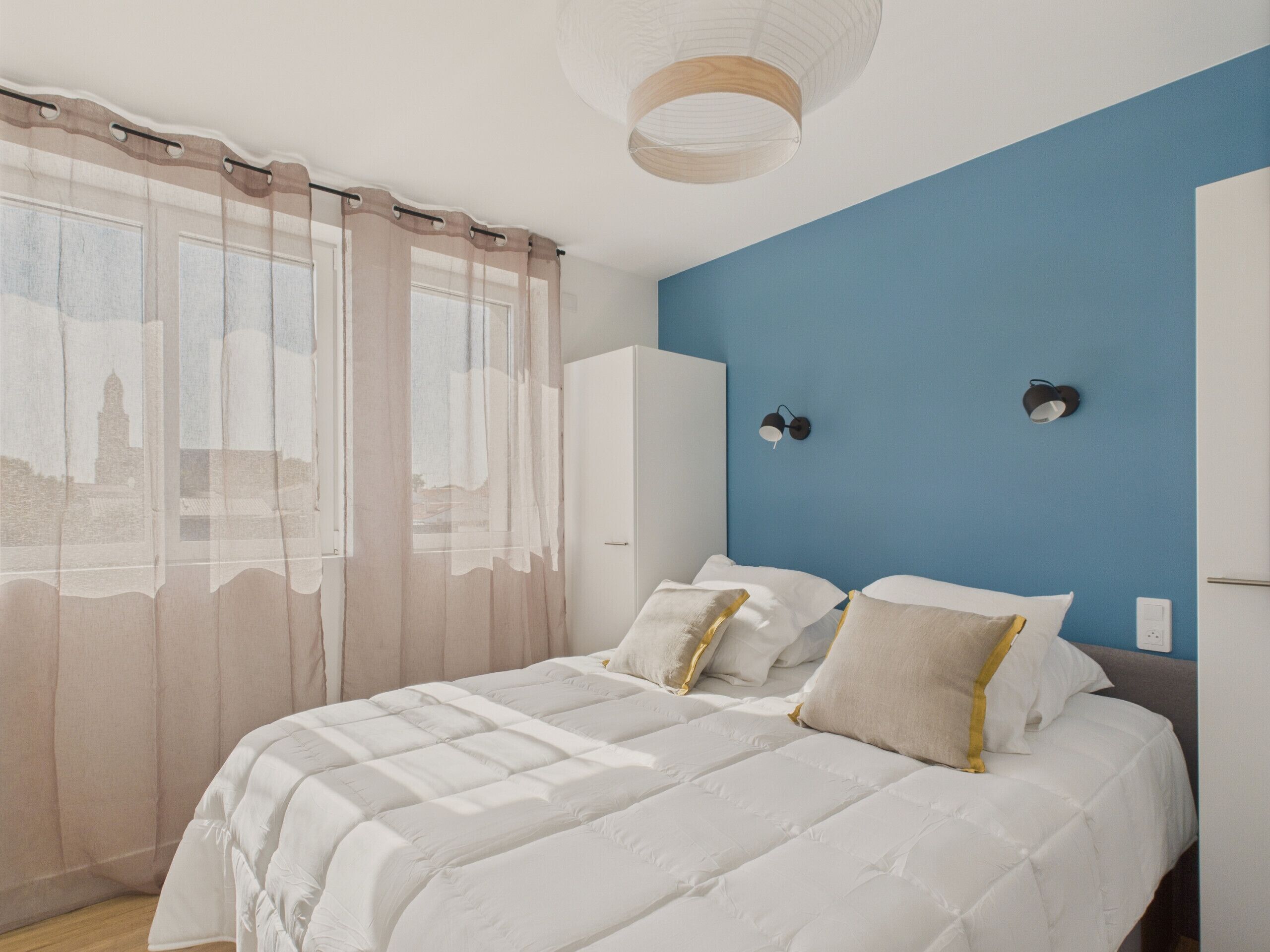 A bedroom with a bed, curtains, a wardrobe, and a blue wall.