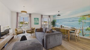 Una sala de estar moderna con un sofá, sillones, una mesa de comedor y un mural con una escena costera.
