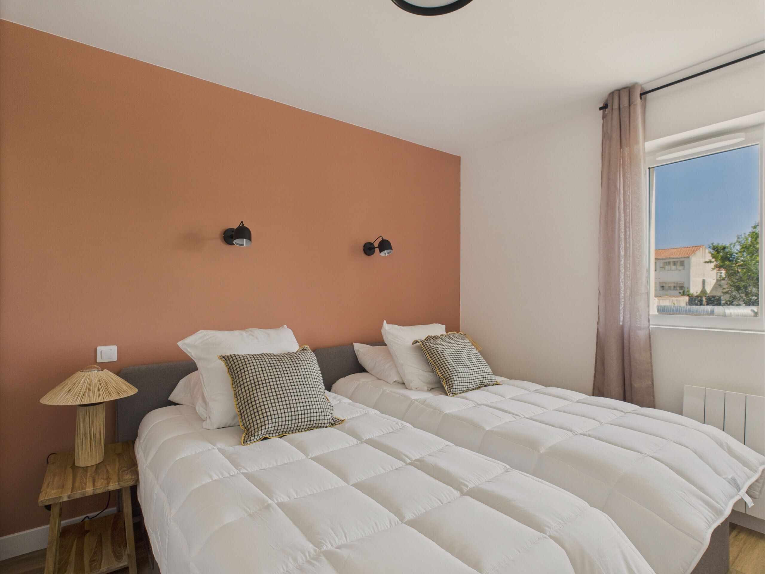 A bedroom with a large bed, two wall-mounted lamps, and a window with curtains.