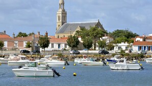 Un puerto deportivo con varias embarcaciones amarradas, una iglesia con campanario y edificios de techos rojos.